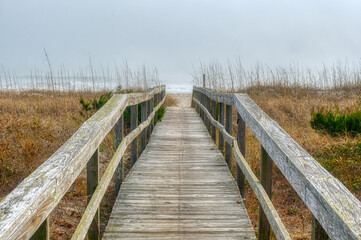 A wooden boardwalk landscape over the grassy sand dunes at a foggy Kure Beach in Wilmington, North Carolina in HDR.