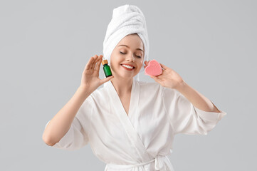 Beautiful young woman with heart-shaped sponge and serum after shower on light background