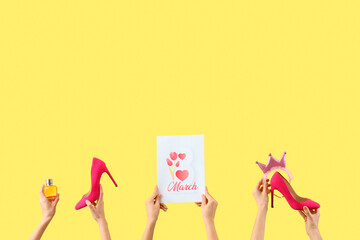 Female hands with festive postcard, high heel shoes and perfume on yellow background. International Women's Day celebration