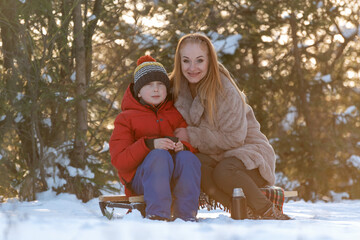 Fototapeta na wymiar Mother and son sitting on sled in winter forest. They are smiling.