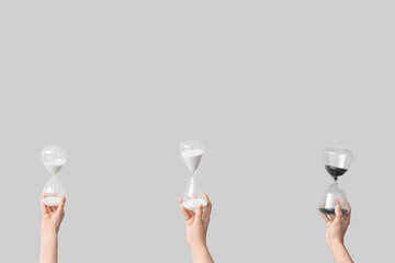 Female hands holding hourglasses on grey background