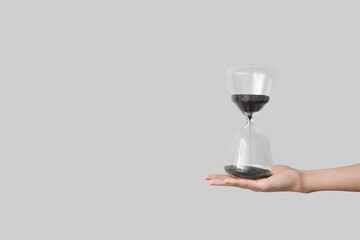 Female hand holding hourglass on grey background