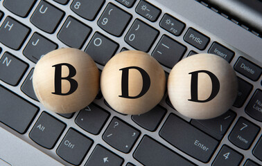 BDD - acronym on wooden balls on laptop keyboard background