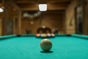 Background of a white cue ball on a green pool table in a rustic cabin ready to be hit to start the game with copy space