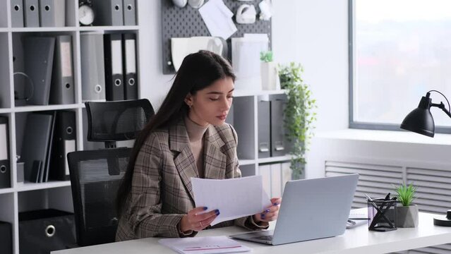 Focused Caucasian woman working with papers and laptop in the modern office. Planning budget, accounting business, calculating taxes.
