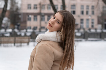 Portrait of long-haired brunette girl in beige sheepskin coat in winter outdoors. Young woman with light makeup on walk