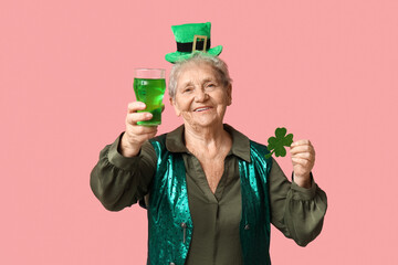 Senior woman in leprechaun hat with glass of beer and clover on pink background. St. Patrick's Day...