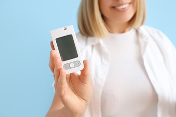 Diabetic woman with glucometer on blue background, closeup