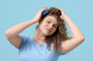 Fototapeta premium Beautiful young woman using hair scalp massager on blue background