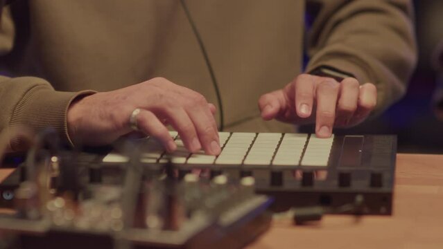 Closeup of male hands of anonymous musician creating beats using sampler at recording studio at night