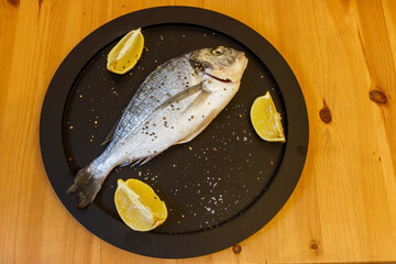 Raw fresh fish dorado with lemon and spices on wooden table. Top view