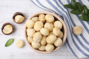 Tasty peeled Macadamia nuts in bowl on light table, flat lay