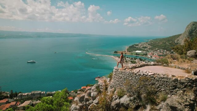High viewpoint of a coastal town Omis with a Cetina river flowing into the sea. Woman enjoying seascape on mountain top. Summer vacation in Croatia.