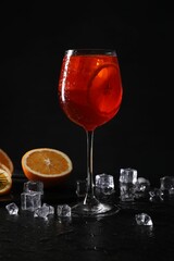 Glass of tasty Aperol spritz cocktail with orange slices and ice cubes on table against black background