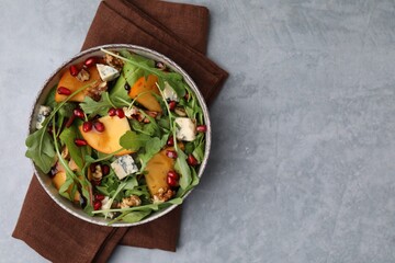 Tasty salad with persimmon, blue cheese, pomegranate and walnuts served on light grey table, top...