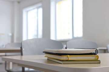 Stack of notebooks on wooden desk in empty classroom. Space for text