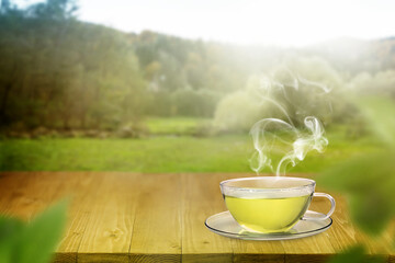 Aromatic green tea in glass cup on wooden table outdoors, space for text