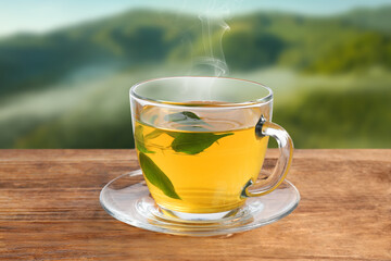 Aromatic green tea in glass cup on wooden table in mountains