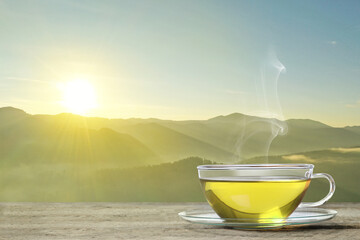 Aromatic green tea in glass cup on wooden table in mountains, space for text