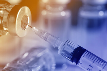 Filling syringe with medicine from vial against blurred background, closeup. Color toned