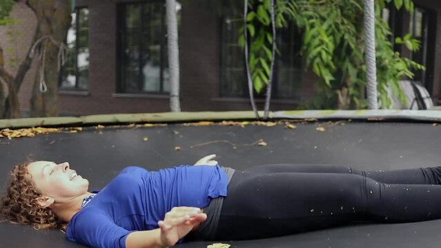 Woman jumps on trampoline attraction in lying position. Slow motion