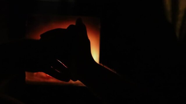 Silhouettes of man and woman hands near burning fireplace. Slow motion