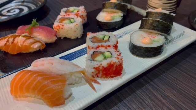 Sushi and rolls in plate. Close-up of sushi rolls on rectangle sushi plate. A set of fresh sushi rolls with salmon, avocado and black sesame seeds served on a plate with chopsticks. Japanese seafood 