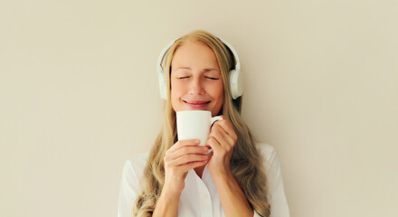 Portrait of happy relaxed middle aged woman listening to music drinking coffee in headphones