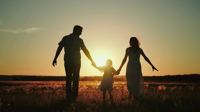 Daddy brings wife with daughter for run in evening field to pick fresh flowers to make bouquet for girls. Daddy and mother run happily with jumping daughter holding hands wishing evening to last