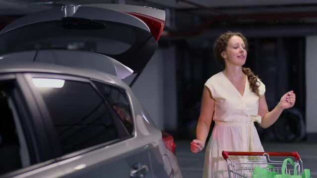 Woman dances near car and shopping cart at underground parking. Slow motion