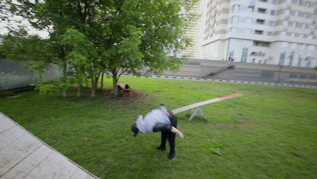 Man does back flip on playground with grass. Slow motion