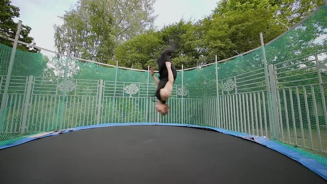 Man jumps on outdoor trampoline and makes flips. Slow motion