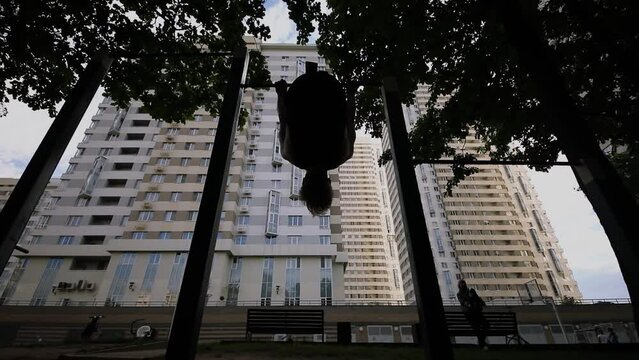 Silhouette of young man which trains on bar near dwelling house. Slow motion
