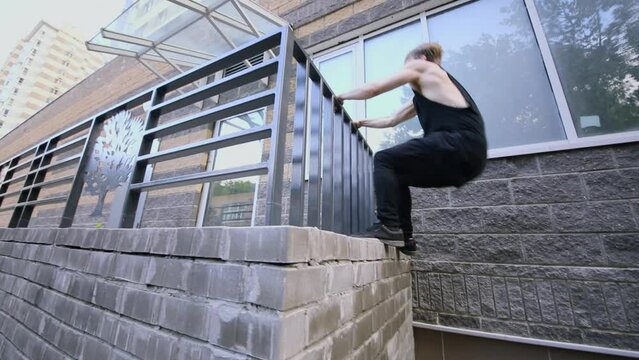 Young man jumps on wall and climbs over handrails near wall. Slow motion