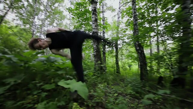 Young man runs and makes flip among plants during parkour training in park. Slow motion