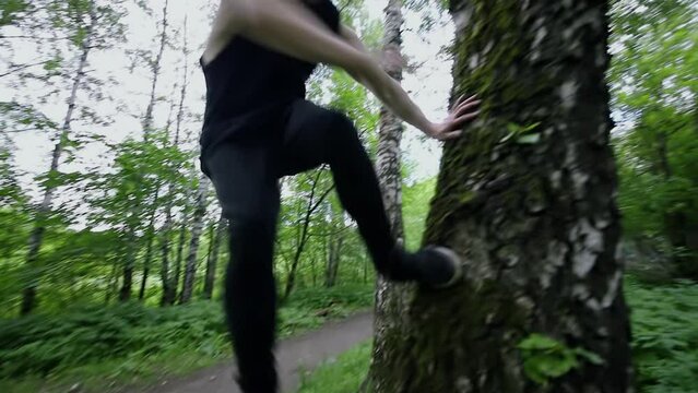 Young man jumps and pushes off from tree during extreme parkour training in park. Slow motion