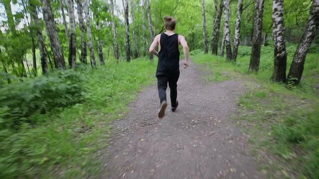 Young man runs and makes somersault during parkour training on alley in park. Slow motion