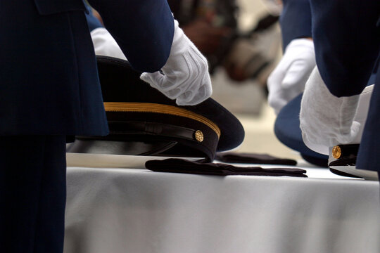 Horizontal close-up with detail of white gloves placing peaked military caps at the US Military table ceremony commemorating Memorial Day in the United States of America.