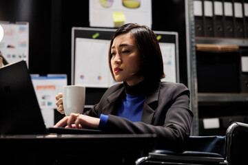 Paralyzed bookkeeping businesswoman manager enjoying cup of coffee and imputing budget plan data on...