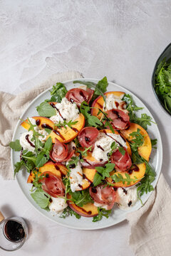 Healthy summer salad with peach, burrata, arugula and jamon
