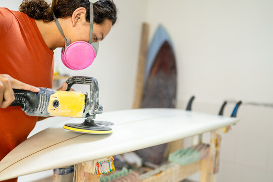 Young latin man polishing a surf board in a workshop