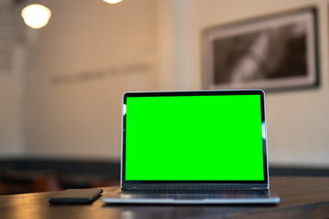 Mockup of laptop computer with empty screen ,ice coffee and smartphone on table side the window in the coffee shop at the cafe,Green screen