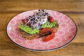 Avocado, egg on brown bread topped with alfalfa on pink plate on wooden table