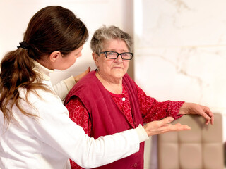 A caring social worker shows and explains something to an elderly woman with hand gestures. Concept...