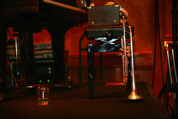 Horizontal backstage close-up of a silver trumpet, trumpet case, piano and piano bench.