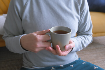 person no face sitting on the floor at home, holding cup of black coffee, cozy home lifestyle, cold at home
