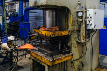 Worker puts iron hot part into press for pressing and quenching