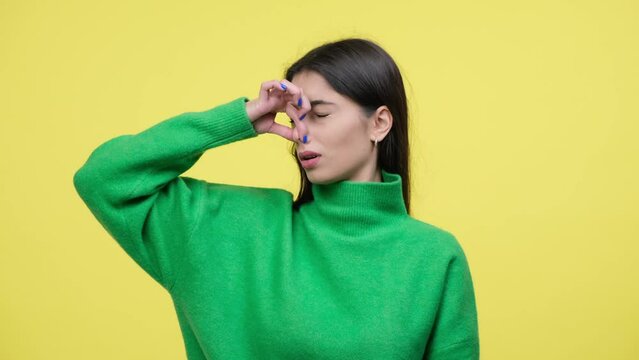 Portrait of a displeased Caucasian woman squeezing nose from a stinky, unpleasant odor on yellow background. Unclean air, nasty smell concept.