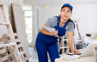 Portrait of a female builder who checks the work done using a laptop