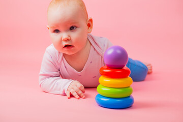 Fototapeta na wymiar baby girl playing with colorful pyramid toy on pink background, closeup